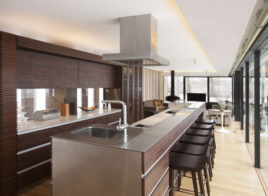Modern kitchen with stainless steel countertops and dark wood cabinetry, featuring a large island with bar stools and a stunning view through floor-to-ceiling windows.