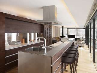 Modern kitchen with stainless steel countertops and dark wood cabinetry, featuring a large island with bar stools and a stunning view through floor-to-ceiling windows.