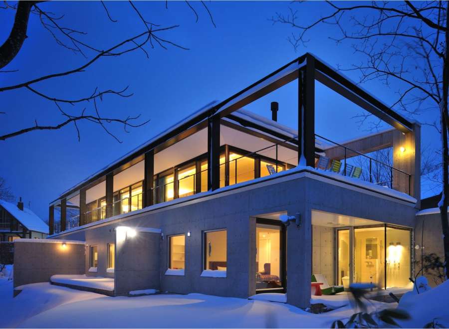 Stunning modern home nestled in a snowy landscape, featuring a sleek concrete exterior and expansive windows offering breathtaking views.