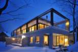 Stunning modern home nestled in a snowy landscape, featuring a sleek concrete exterior and expansive windows offering breathtaking views.