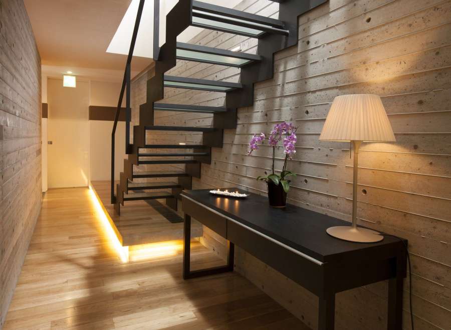 Modern hallway with sleek glass and metal staircase, illuminated by warm lighting.