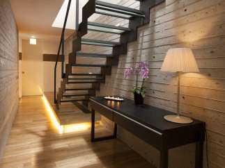 Modern hallway with sleek glass and metal staircase, illuminated by warm lighting.