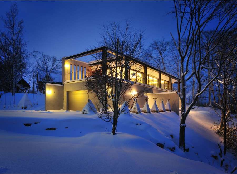 Stunning modern home nestled in a snowy landscape, featuring a sleek design with expansive windows and a spacious garage.