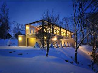 Stunning modern home nestled in a snowy landscape, featuring a sleek design with expansive windows and a spacious garage.