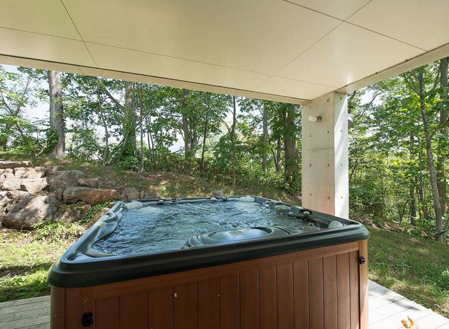 Relax and unwind in your private hot tub, nestled under a covered patio and surrounded by a serene forest backdrop.
