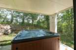 Relax and unwind in your private hot tub, nestled under a covered patio and surrounded by a serene forest backdrop.