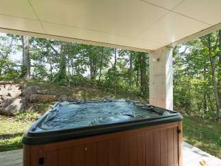 Relax and unwind in your private hot tub, nestled under a covered patio and surrounded by a serene forest backdrop.