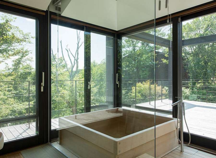 Luxurious bathroom with a wooden bathtub and floor-to-ceiling windows offering breathtaking views of nature.