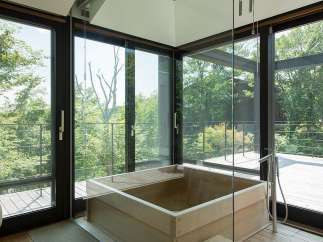 Luxurious bathroom with a wooden bathtub and floor-to-ceiling windows offering breathtaking views of nature.