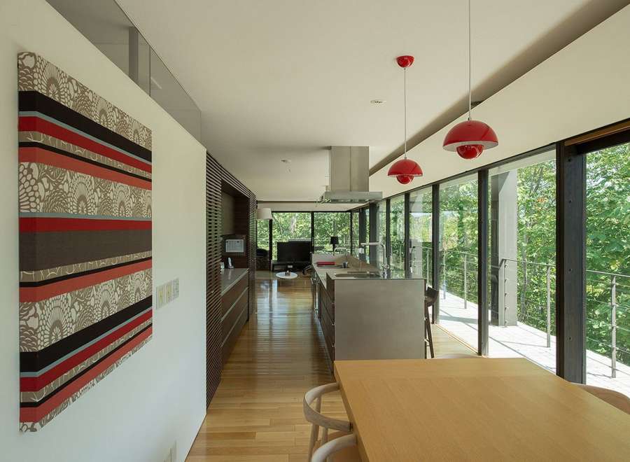 Modern house with open floor plan, hardwood floors, and floor to ceiling windows showcasing a lush green landscape.