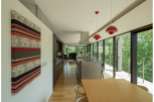 Modern house with open floor plan, hardwood floors, and floor to ceiling windows showcasing a lush green landscape.