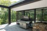 Modern outdoor kitchen with stainless steel grill and woodpile, perfect for summer barbecues.