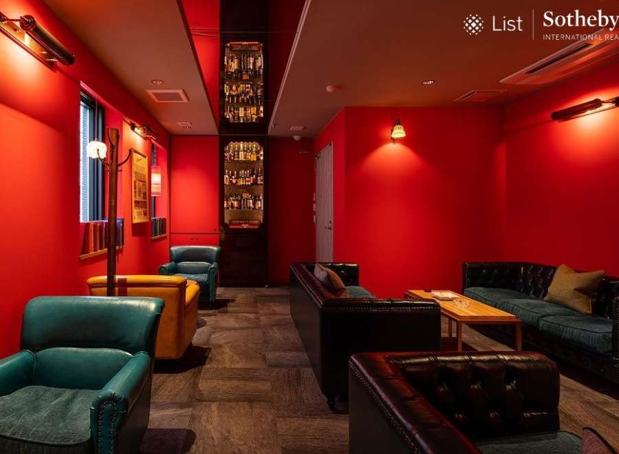 Luxurious red-walled lounge with plush leather seating and a built-in bar showcasing an impressive liquor collection.
