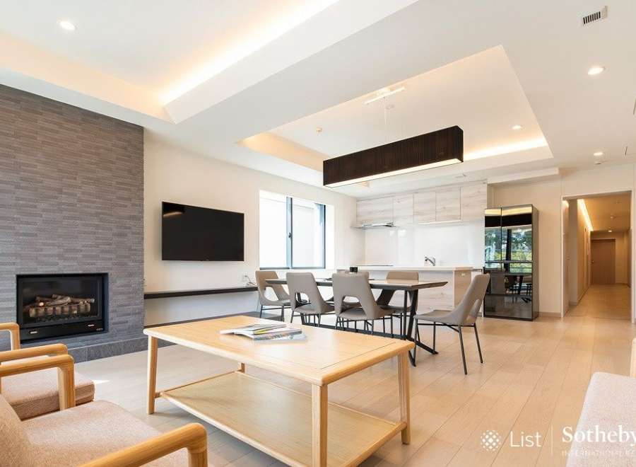 Modern living space with open-plan kitchen and dining area, featuring a sleek fireplace and large windows.