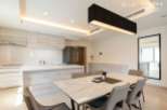 Modern kitchen with sleek cabinetry and island, open to a dining area with marble table and six chairs.