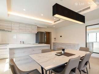 Modern kitchen with sleek cabinetry and island, open to a dining area with marble table and six chairs.