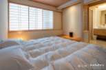 Experience serene living in this exquisitely designed bedroom, featuring a plush, white comforter and traditional Japanese shoji screens that filter soft, natural light.