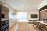 Modern kitchen with sleek black appliances and light wood cabinetry opens to a dining area with a marble table and comfortable seating.