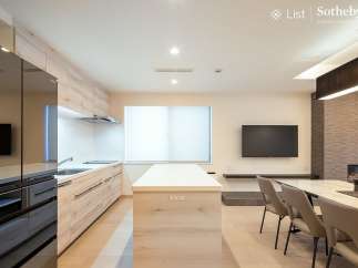Modern kitchen with sleek black appliances and light wood cabinetry opens to a dining area with a marble table and comfortable seating.