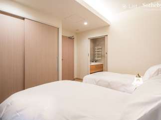 This luxurious bedroom features twin beds with crisp white linens, a built-in closet with sliding doors, and an ensuite bathroom with modern fixtures.