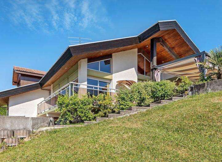 Stunning contemporary home nestled on a hillside, boasting expansive windows and a spacious outdoor terrace.
