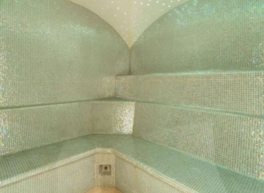 Relax and rejuvenate in this luxurious steam room, featuring stunning iridescent mosaic tile and a calming, softly lit atmosphere.