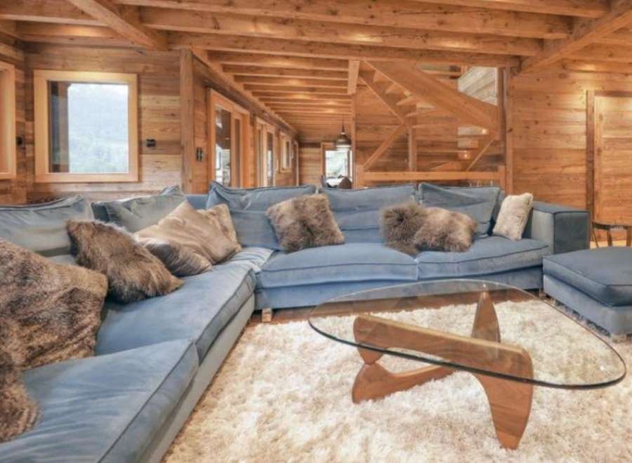 Luxurious chalet living room with a stunning wooden interior, featuring a large comfortable sectional sofa and a stylish glass coffee table.