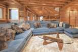 Luxurious chalet living room with a stunning wooden interior, featuring a large comfortable sectional sofa and a stylish glass coffee table.