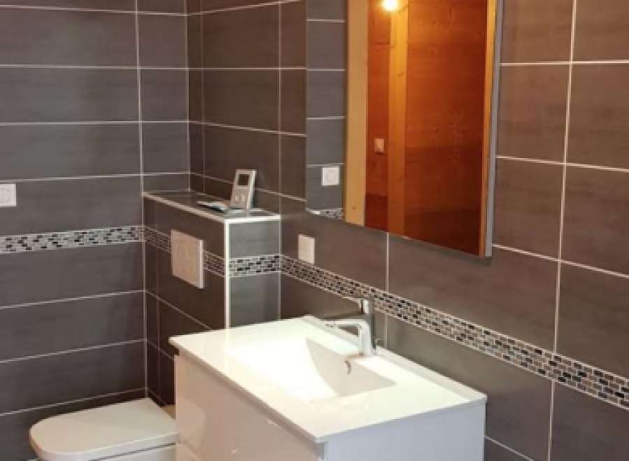 Modern bathroom with dark gray tiles, white vanity, and a built-in toilet.