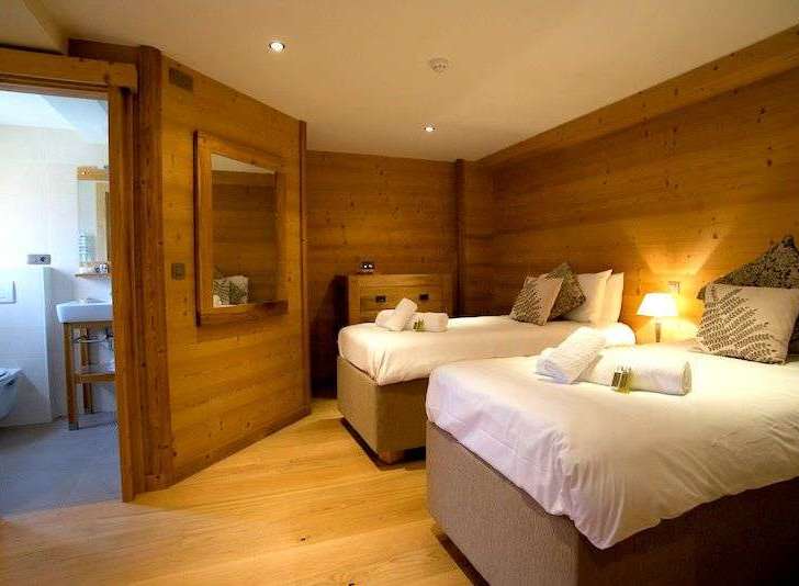 Cozy chalet bedroom with twin beds, ensuite bathroom, and wooden walls.