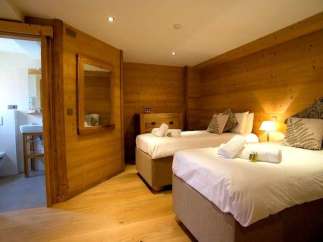 Cozy chalet bedroom with twin beds, ensuite bathroom, and wooden walls.