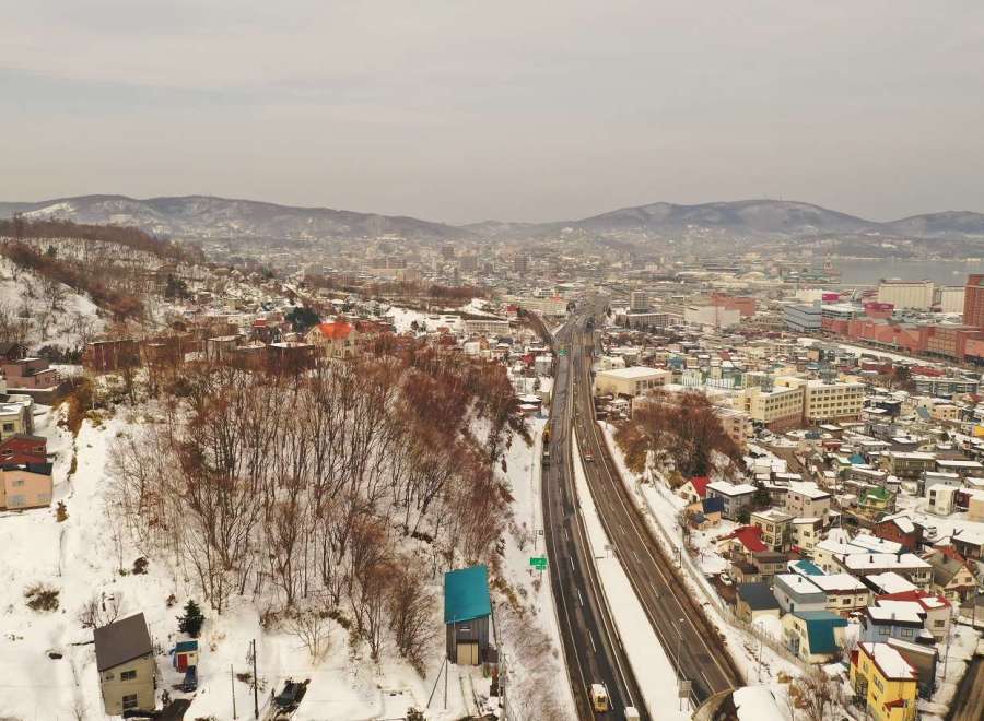 Explore the stunning winter landscape of Otaru, Japan, with this aerial view showcasing a modern highway cutting through a snow-covered town.