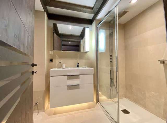 Modern bathroom with a walk-in shower, sleek white vanity, and elegant wood beam ceiling.