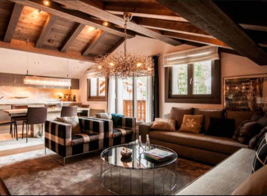 This stunning chalet boasts a spacious open-plan living area with exposed wooden beams and a cozy fireplace, creating a warm and inviting atmosphere.