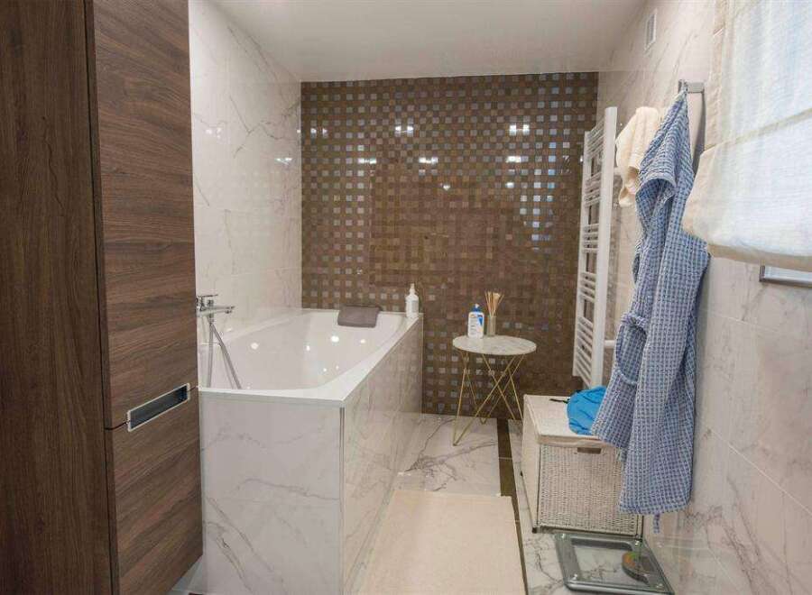 Luxurious bathroom with a freestanding bathtub, marble flooring, and a stylish mosaic tile feature wall.