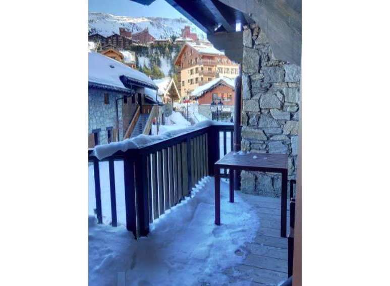 Experience the charm of a winter wonderland from this property's balcony, offering stunning views of a snow-covered village nestled in the mountains.