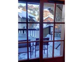 Experience the charm of a winter wonderland from this property's balcony, offering stunning views of snow-covered chalets and a picturesque mountain village.