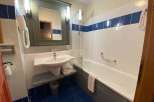 This bathroom features a clean and modern design with white tiles and a blue accent stripe.