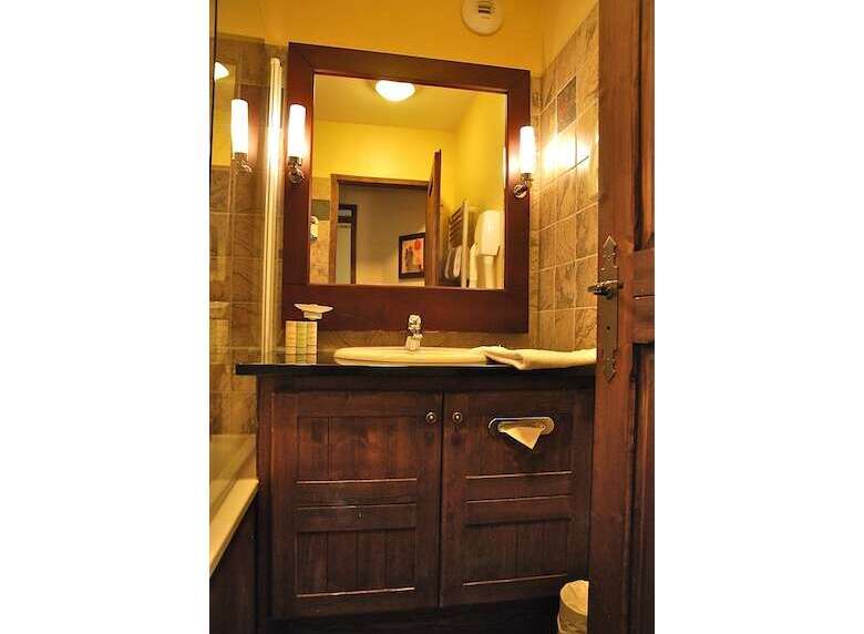 This charming bathroom features a rustic wooden vanity with ample storage, complemented by a large mirror with elegant sconce lighting.