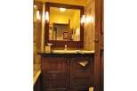 This charming bathroom features a rustic wooden vanity with ample storage, complemented by a large mirror with elegant sconce lighting.