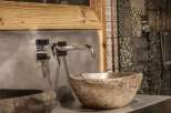 This bathroom boasts a unique stone sink and a sleek chrome faucet, creating a modern yet natural aesthetic.