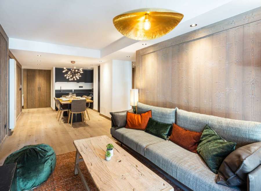 This stunning apartment boasts a spacious open-plan living area with a cozy sofa and plush pillows, perfect for relaxing after a day on the slopes.