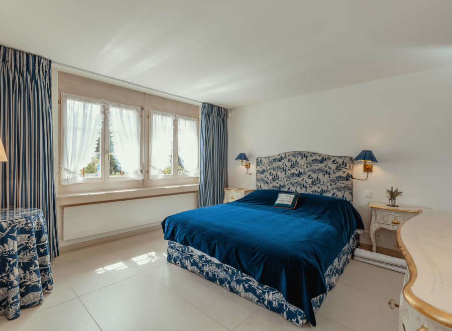 This elegant bedroom features a luxurious blue velvet bed, complemented by matching patterned curtains and a headboard.