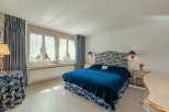 This elegant bedroom features a luxurious blue velvet bed, complemented by matching patterned curtains and a headboard.