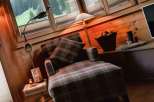 Cozy up in this charming cabin retreat! Enjoy the warmth of the wooden interior and the comfort of the plaid armchair.