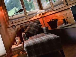 Cozy up in this charming cabin retreat! Enjoy the warmth of the wooden interior and the comfort of the plaid armchair.