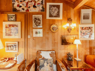 This cozy cabin interior features warm wood paneling and a unique cowhide armchair, creating a rustic yet inviting atmosphere.