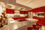 This modern kitchen boasts sleek red cabinetry and a spacious island with a cooktop, perfect for culinary enthusiasts.