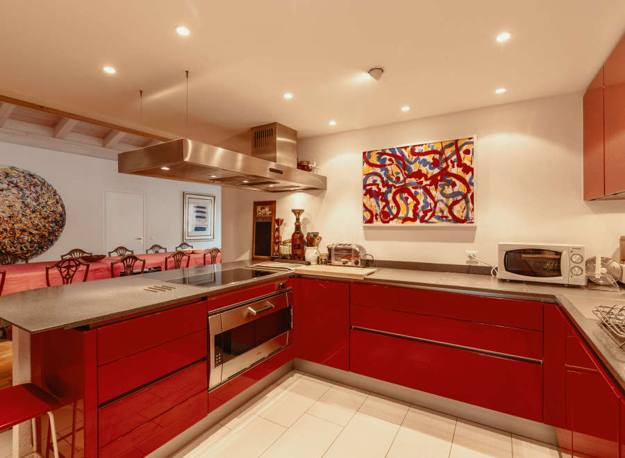 This modern kitchen boasts sleek red cabinetry and a stainless steel range hood, creating a stylish and functional space.