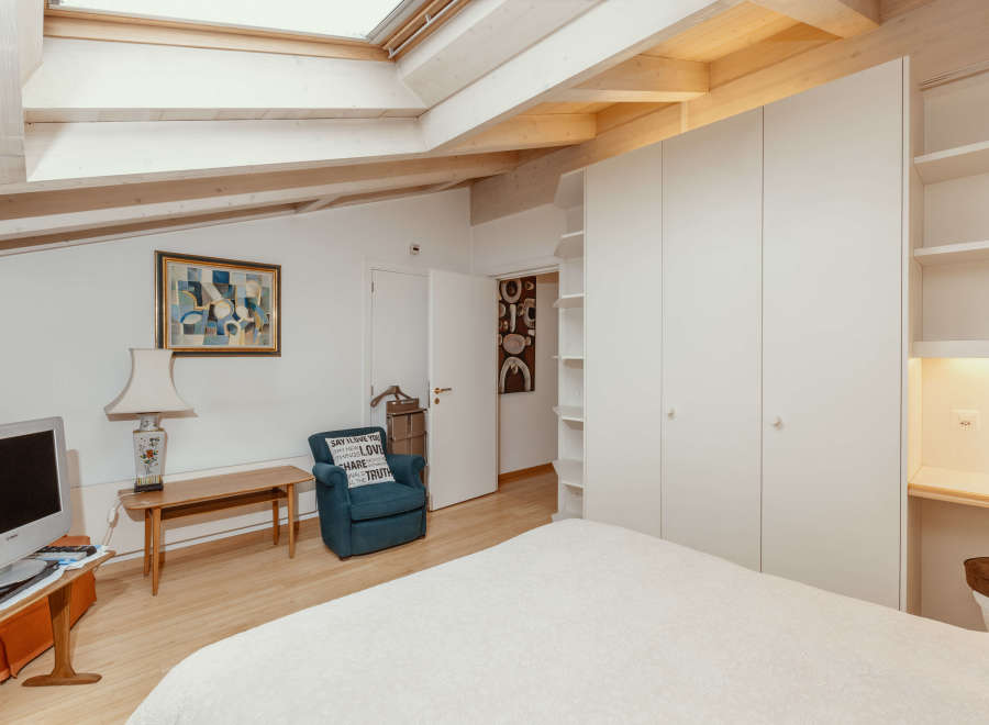 This charming bedroom features a unique architectural design with exposed wooden beams and a skylight, creating a bright and airy atmosphere.